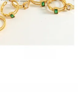 Detail of gold braided twist rings featuring emerald cut green and white zircon stones