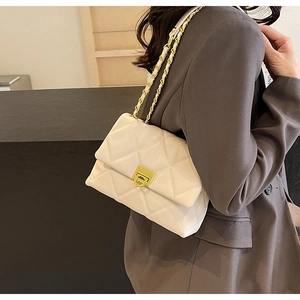 Detail of cream quilted crossbody bag featuring a gold chain strap and metallic lock