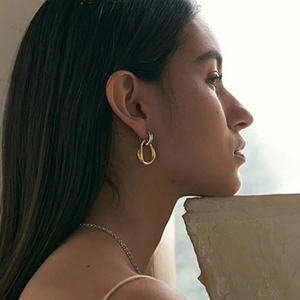Close-up of interlocking gold and silver geometric hoop earrings on a female model