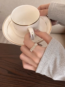 Close-up of a silver floral open ring on a model holding a coffee cup for an elegant look