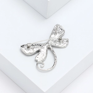 Back view of silver dragonfly brooch with detailed texture and pin clasp on white pedestal