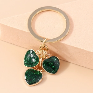 Close-up of golden keychain featuring three dark green glitter heart pendants on beige stand