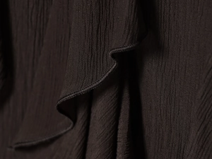 Détail de jupe à volants marron foncé montrant la texture plissée et le tissu crêpe