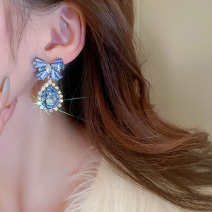 Macro detail of sparkling blue crystal bow and teardrop clip-on earrings on model