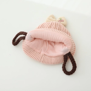 Détail du bonnet tricoté rose pour bébé avec broderie cerise et tresses cache-oreilles
