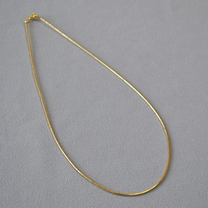 Primo piano di una collana girocollo dorata minimalista su superficie grigia strutturata