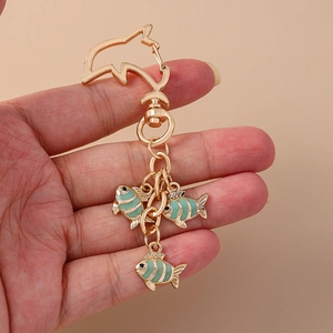 Detail of gold fish-shaped keychain with mint green enamel pendants and intricate metal link