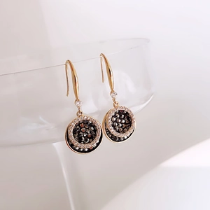 Detail view of gold circular drop earrings with black and white pavé crystal inlay