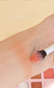 Gros plan du pinceau estompeur appliquant du maquillage rose sur la peau du bras