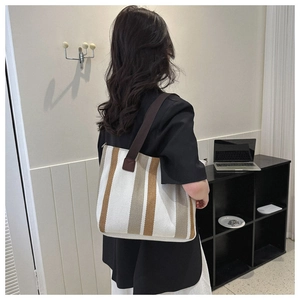 Brown and white striped canvas tote bag worn by a model in a modern room setting