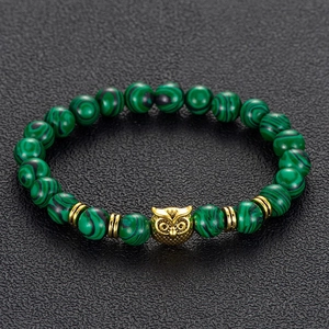 Close-up of green malachite beads and golden owl charm on black textured surface