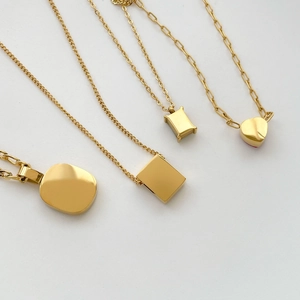 Detail of four golden titanium necklaces featuring geometric and heart-shaped pendants