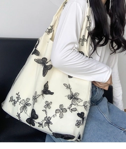 Detail of floral butterfly embroidery on a beige canvas tote bag worn by a model