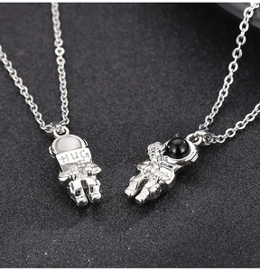 Macro shot of silver astronaut couple pendants with Hug Me sign and tiny rose detail