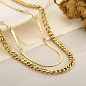 Détail du collier superposé avec chaîne cubaine dorée et chaîne serpent sur fond blanc