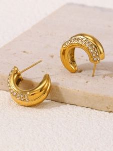 Detail of gold double C-shaped earrings with rows of zircon on a beige textured stone