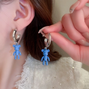 Close-up of blue bear pendant earrings on silver hoop showing glossy texture and details