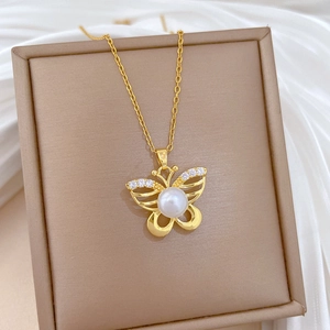 Golden butterfly necklace with pearl and crystal details on beige jewelry box