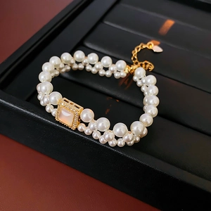 Detail of 18k gold plated double-layer pearl bracelet with square charm and leaf pendant