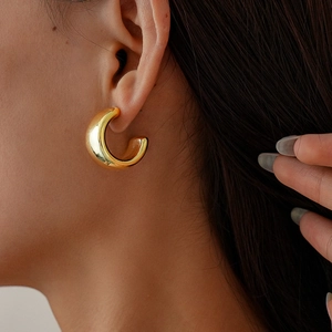 Close-up of a minimalist golden C-shaped geometric earring worn by a model