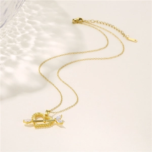 Collana dorata con ciondolo a cuore e freccia con zirconi su sfondo beige minimalista