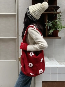 Borsa tote rossa in peluche con fiori bianchi indossata in un interno accogliente