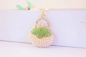 Close-up of golden handbag keychain with green rhinestones and white pearls detail