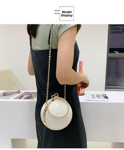 Detail of white spherical evening bag featuring rhinestone ring handle and golden chain