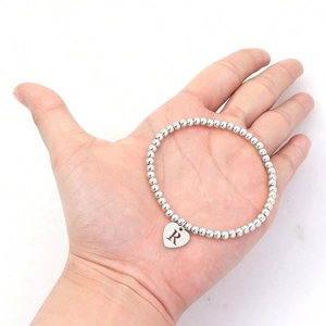 Detailed close-up of a silver beaded heart bracelet with engraved letter R on a hand