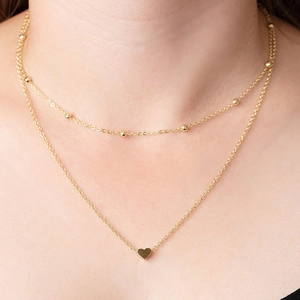 Dettaglio di una collana dorata a due strati con ciondolo a cuore e piccole perline