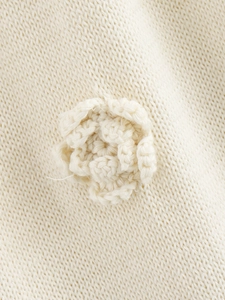 Detail of hand-crocheted 3D flower applique on beige knitted sleeveless dress fabric