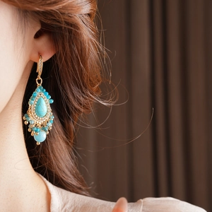 Détail de boucles d'oreilles bohèmes avec gouttes de turquoise et cristaux dorés fins