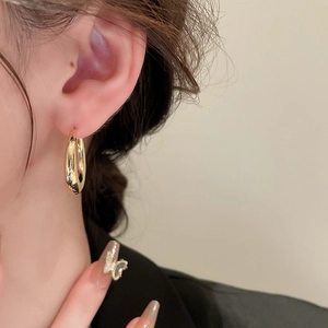 Close-up of a gold water-drop C-shape metal earring worn on a model with skin texture