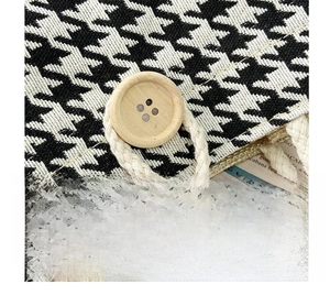 Detail of houndstooth canvas bag featuring a round wooden button and woven rope loop closure