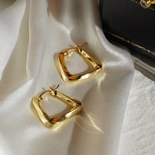 Detailed view of twisted square hoop earrings in gold finish on white silk background