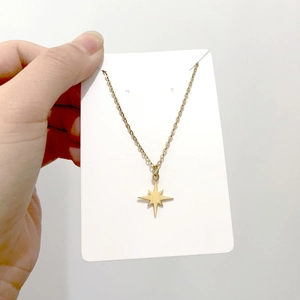 Detailed view of a gold starburst pendant necklace held on a minimalist white card display