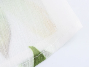 Gros plan sur un tissu en mousseline blanche avec imprimé floral vert et couture d'ourlet
