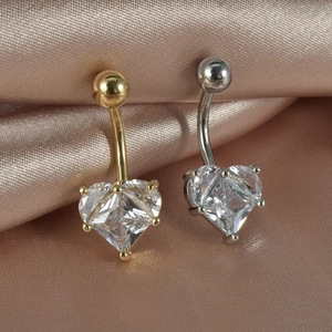 Pair of heart-shaped zircon belly button rings in gold and silver on silk background