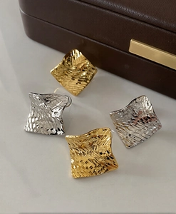 Detailed macro view of textured rhombus earrings in polished gold and silver finishes