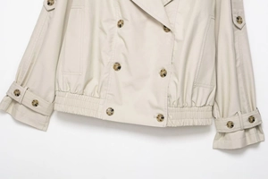 Detail of beige waterproof windbreaker jacket showing amber buttons and elastic hem