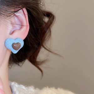 Macro detail of layered heart earrings with blue denim fabric and brown resin center