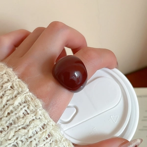 Detail of a dark reddish-brown resin round ring worn on a finger holding a coffee cup