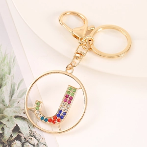 Detailed shot of golden alphabet J keychain with colorful rhinestones on a white plate