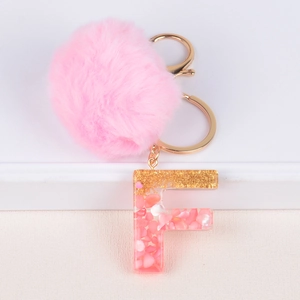 Close-up of pink pompom keychain with resin letter F and gold foil details on white base