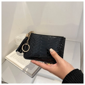 Detail of glossy black crocodile pattern mini purse with gold zipper and tassel keychain