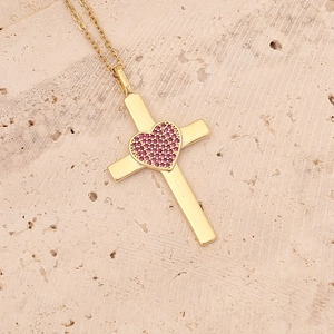 Close-up of gold cross necklace with pink heart zircon pendant on stone background
