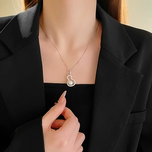 Detail of silver gourd pendant featuring zircon stones and a central pearl on a model