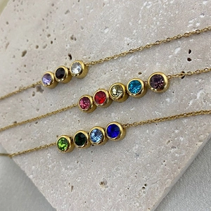 Detailed shot of three gold-plated necklaces with colorful birthstone bar pendants on stone