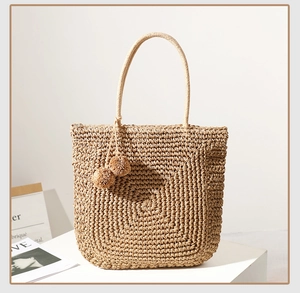 Detail of hand-woven straw tote bag with soft decorative pom-poms and sturdy handles