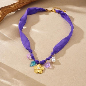 Detail of purple fabric chain necklace with gold flower pendant and baroque pearl accents
